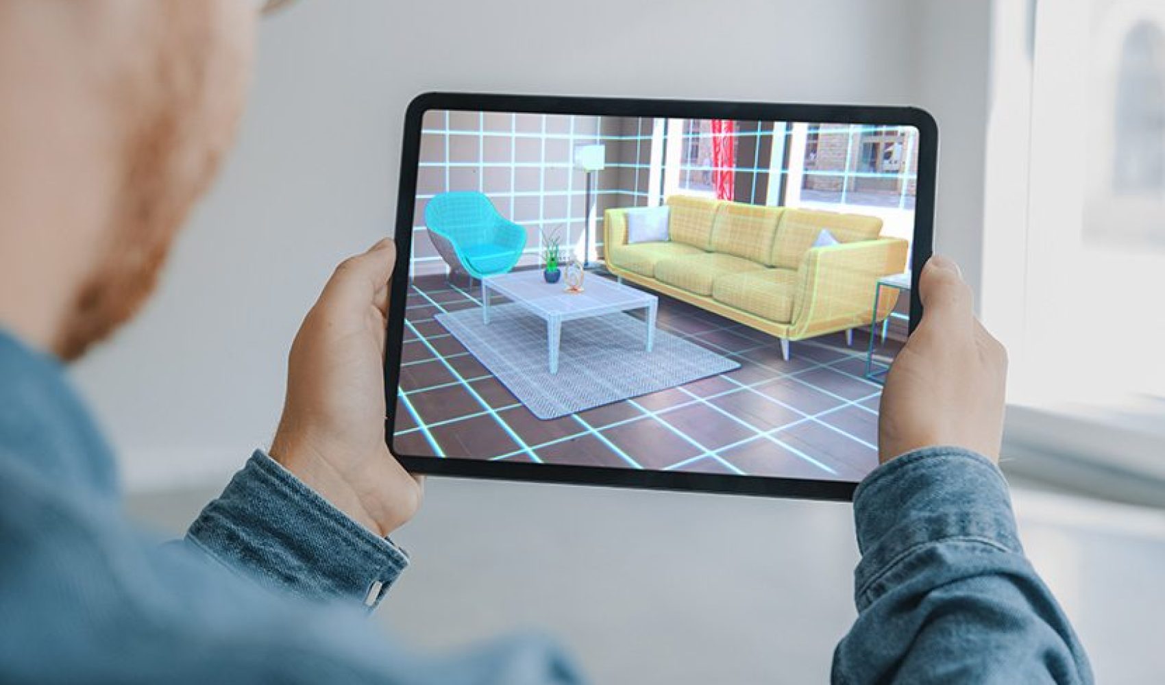 Decorating Apartment: Man Holding Digital Tablet with AR Interior Design Software Chooses 3D Furniture for Home. Man is Choosing Sofa, Table for Living Room. Over Shoulder Screen Shot with 3D Render Decorating Apartment: Man Holding Digital Tablet with AR Interior Design Software Chooses 3D Furniture for Home. Man is Choosing Sofa, Table for Living Room. Over Shoulder Screen Shot with 3D Render